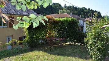 A house with a tiled roof, surrounded by greenery and a grassy yard.