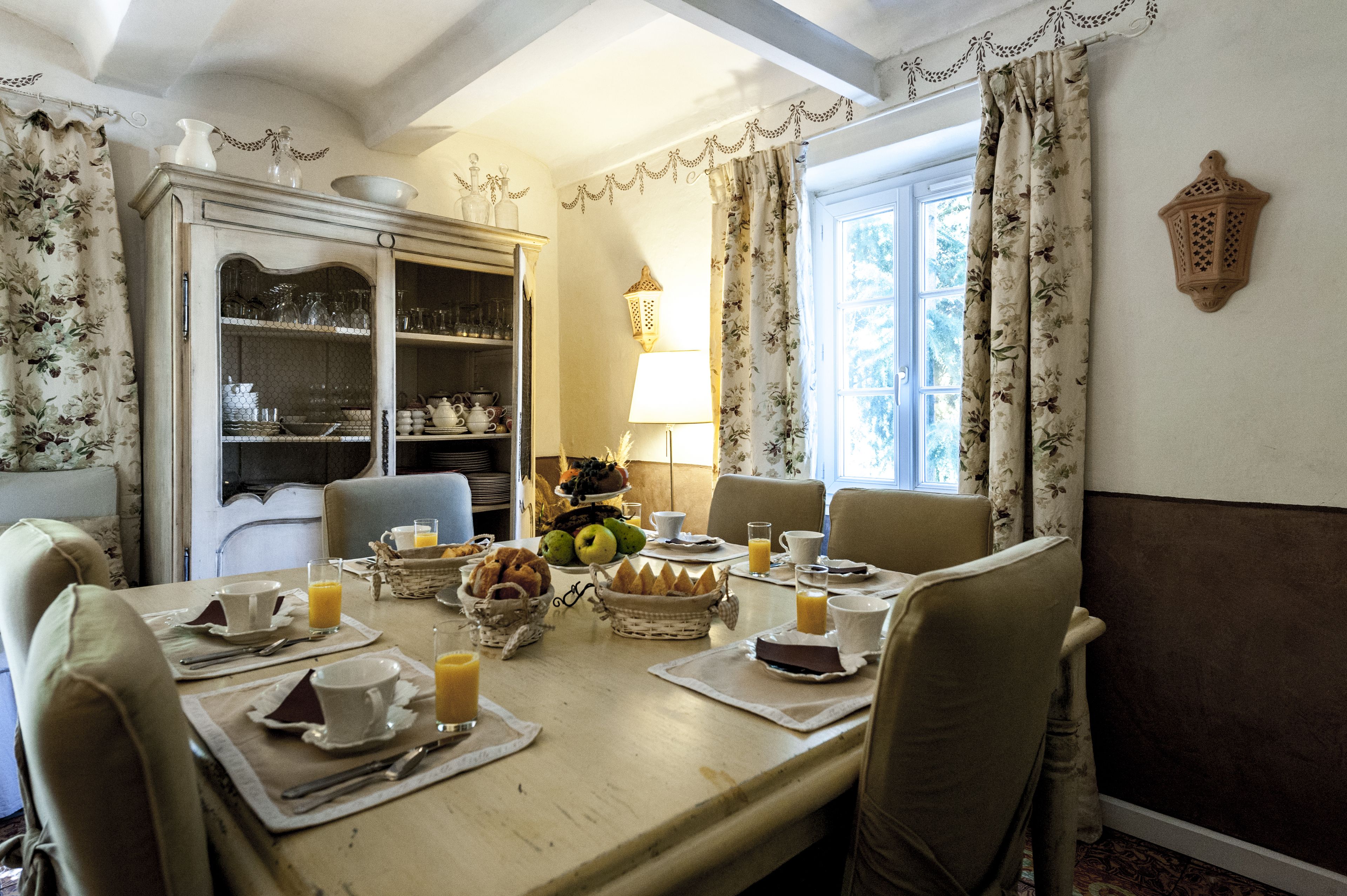 A dining room with a table set for breakfast, including plates, cups, and a fruit basket.