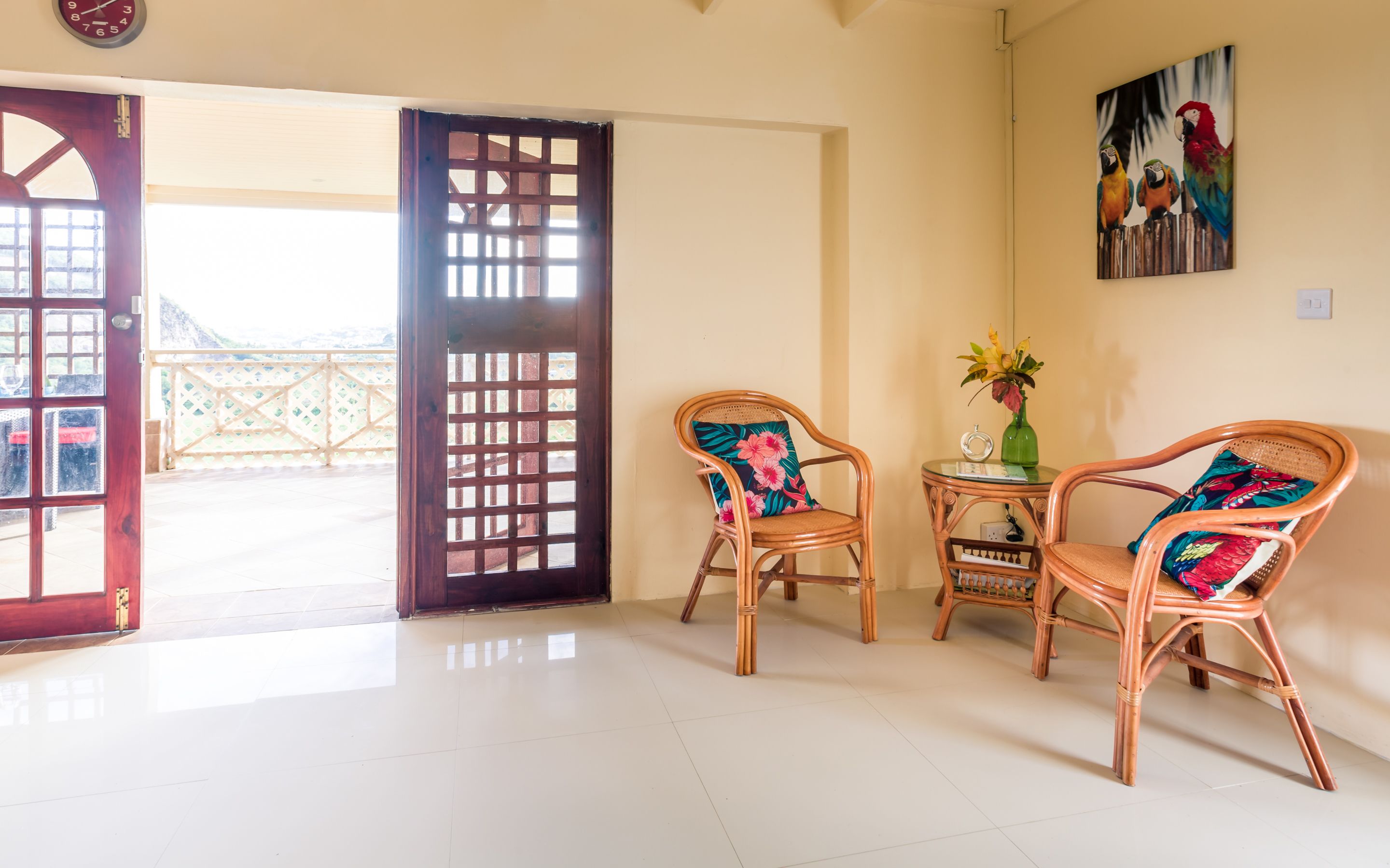 A room with two wicker chairs, a small table with a vase, and a door leading outside.