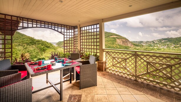 An outdoor patio with wicker furniture, a table set for dining, and a view of a mountainous landscape.