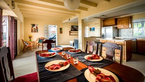 A dining area with a wooden table set for four, a kitchen with modern appliances, and a living area with a sofa and artwork. - Flamboyant Villa (Gros Islet)