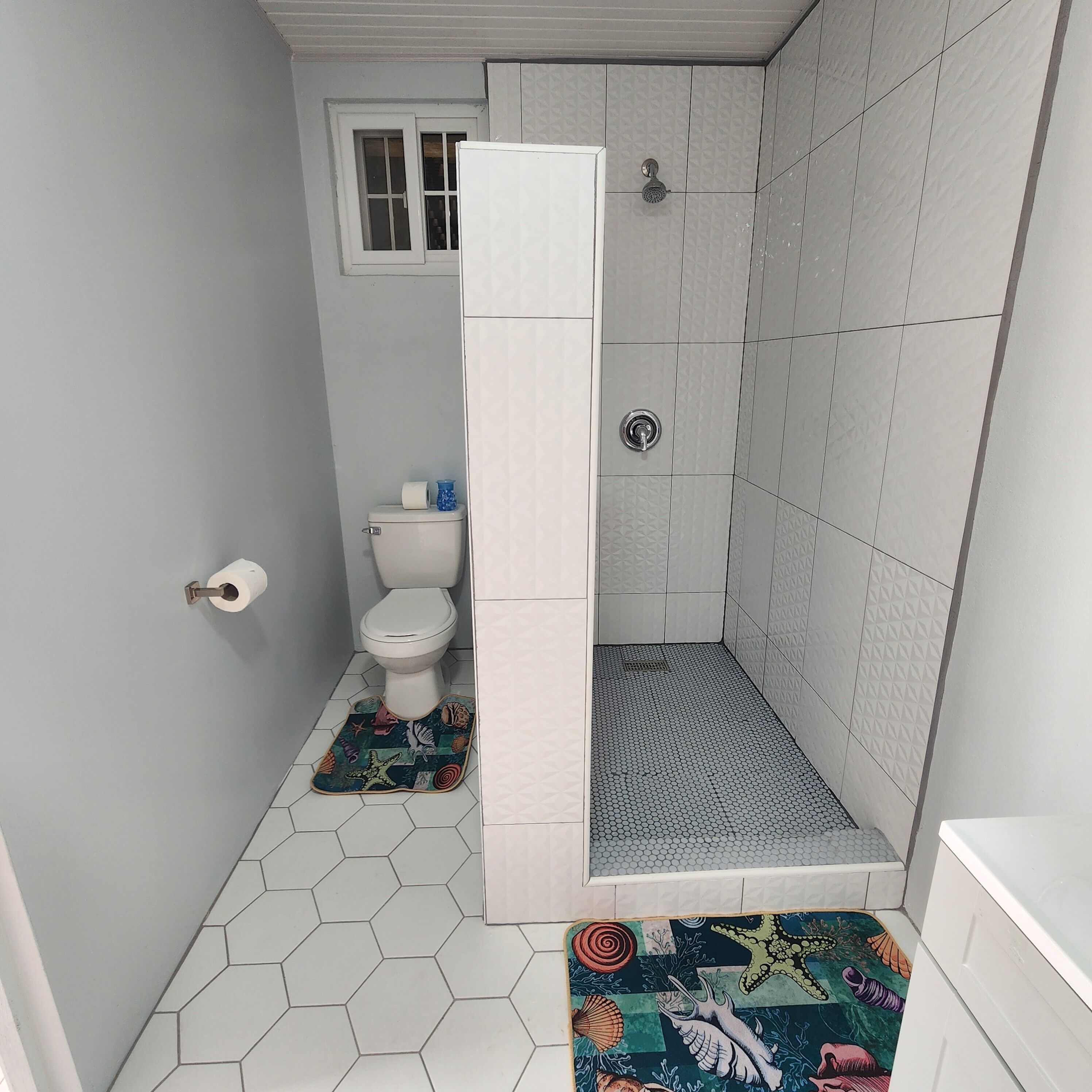 Un baño pequeño con inodoro, ducha y suelo de baldosas hexagonales.