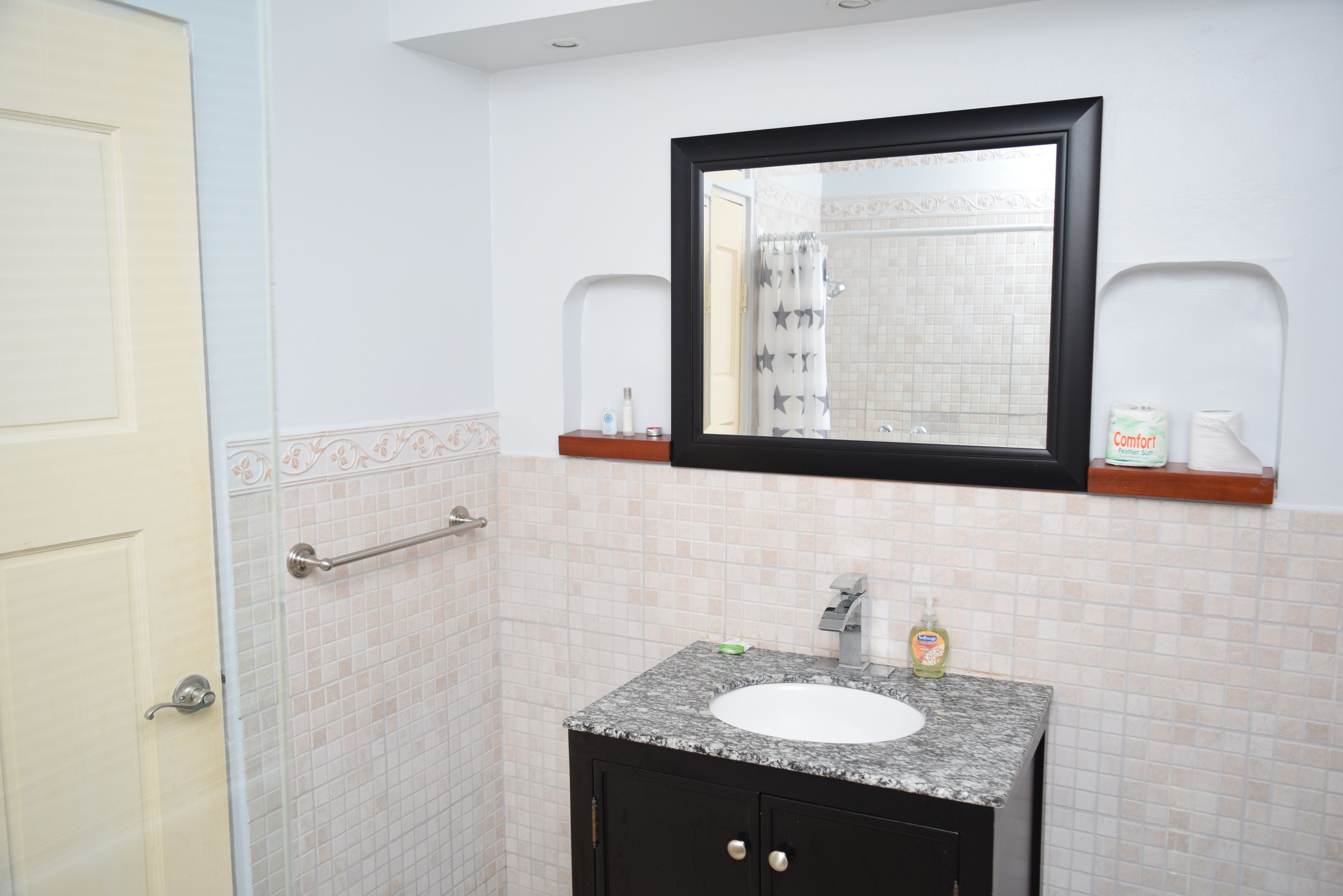 A bathroom with a white door, a sink with a mirror above it, and a shower curtain with star patterns.
