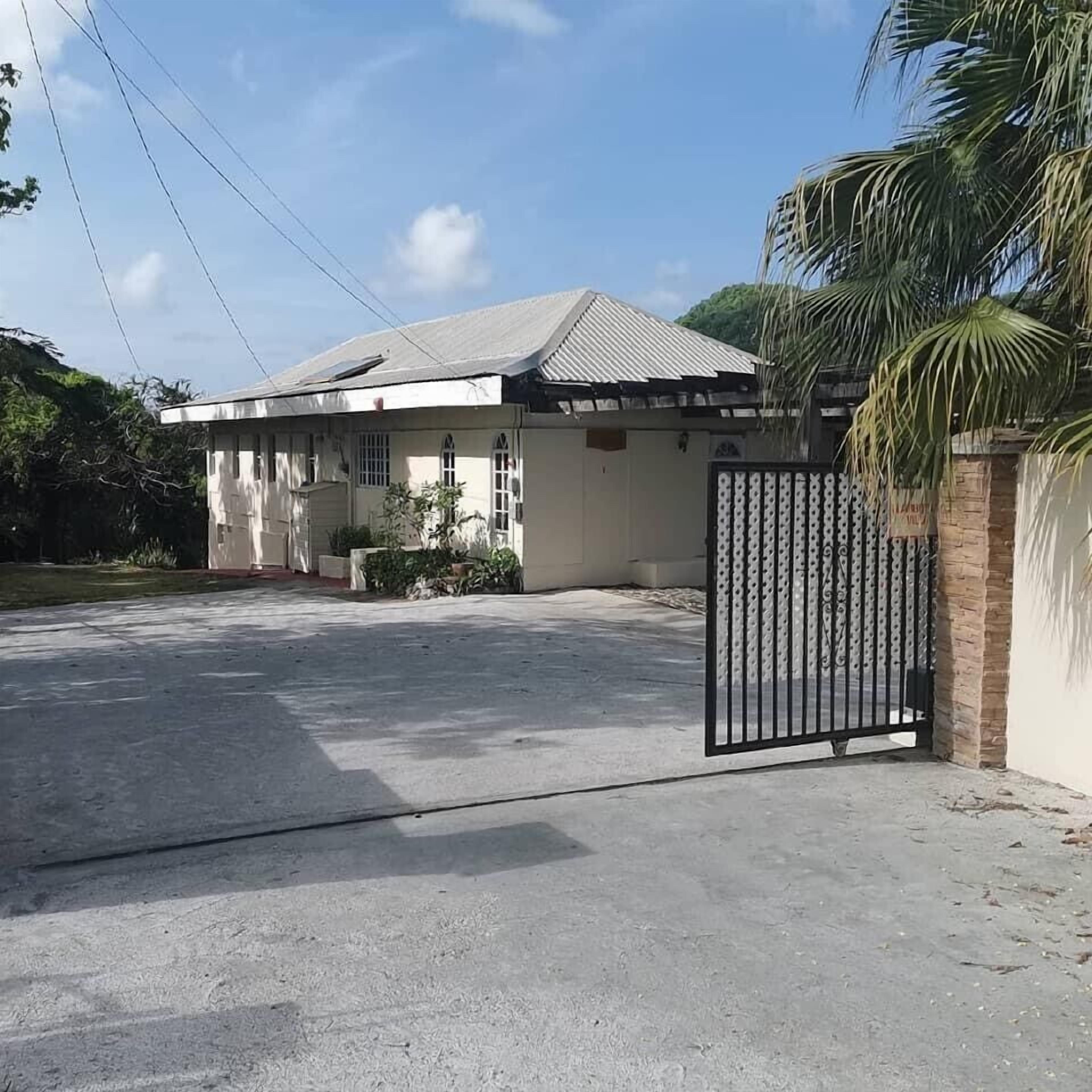 A single-story house with a gated entrance, a concrete driveway, and a small garden area.