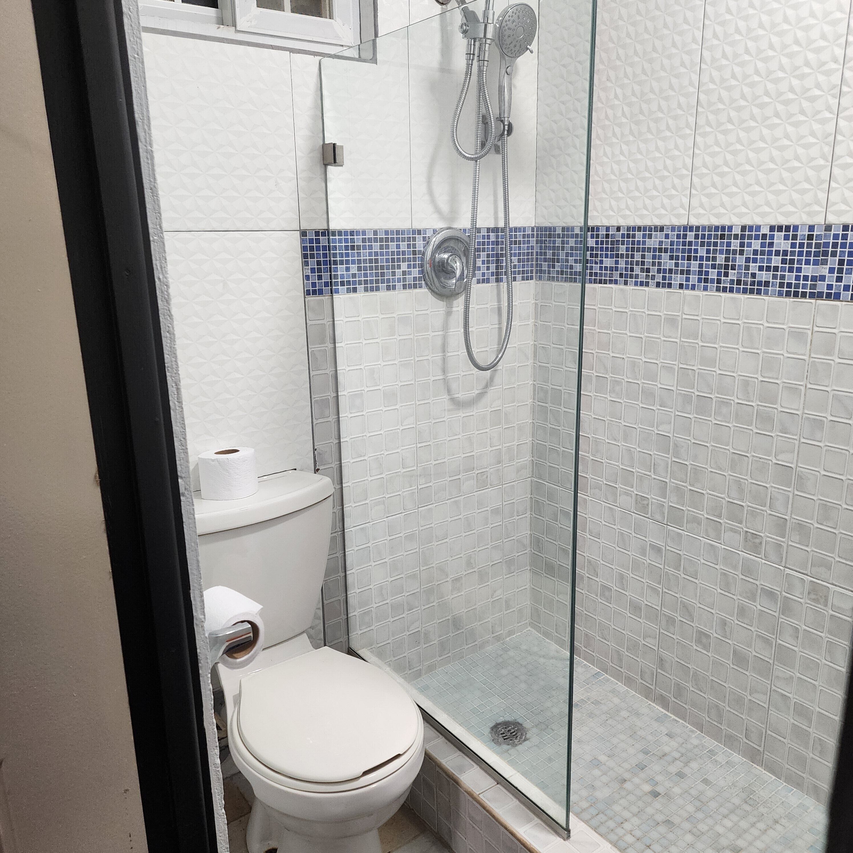 Une salle de bain comprenant des toilettes, une douche en verre et un mur carrelé orné d’une bordure en mosaïque bleue.