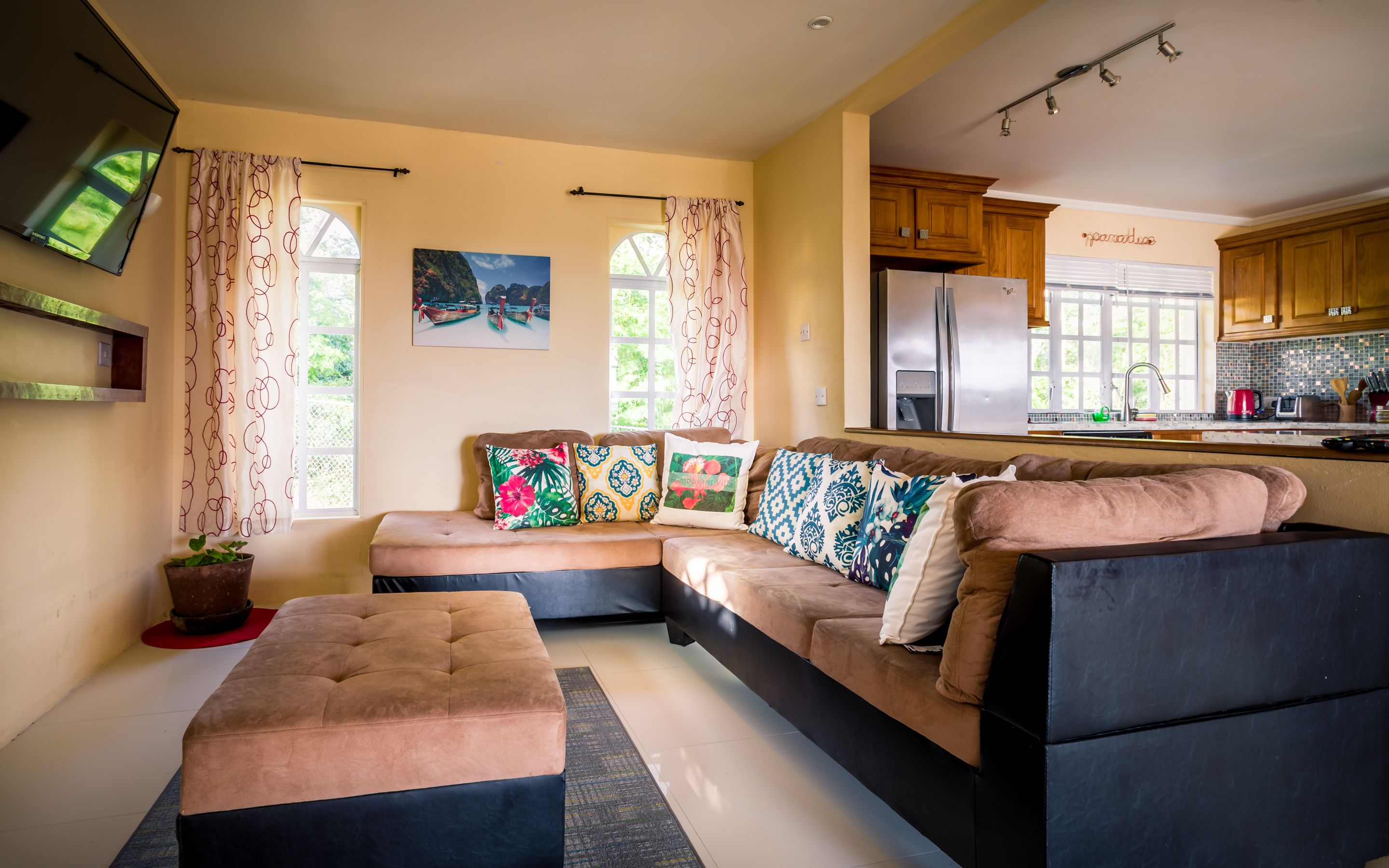 A modern living room with a sectional sofa, a flat-screen TV, and a kitchen with wooden cabinets.