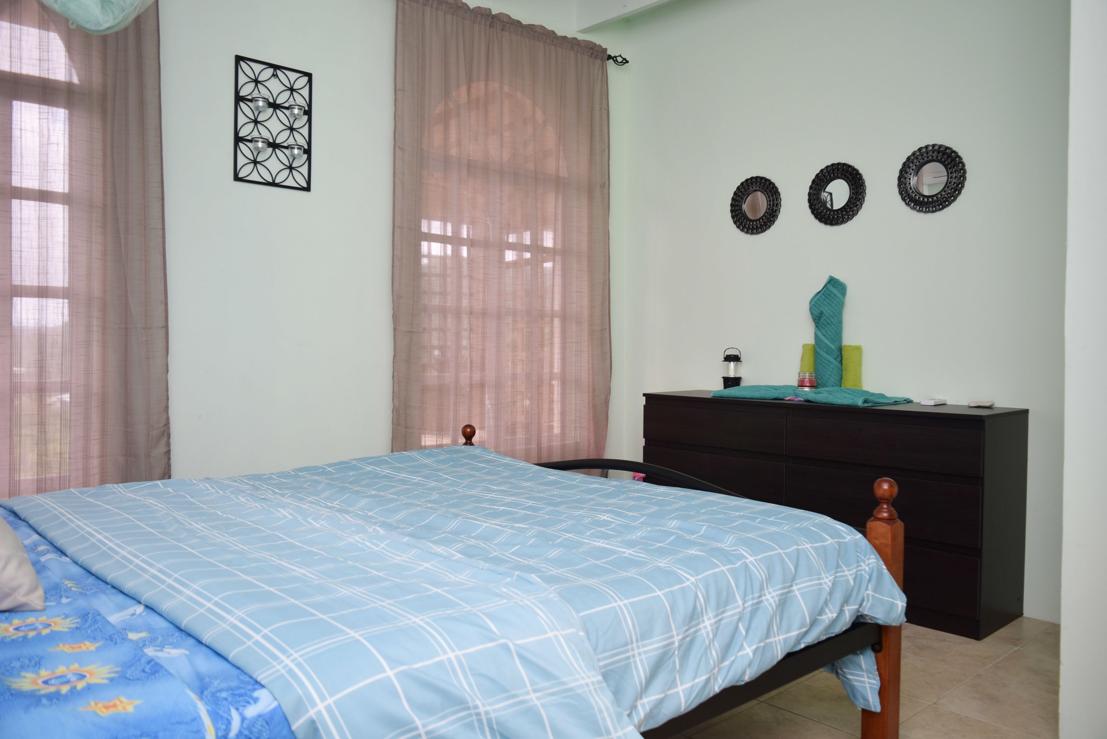 A bedroom with a bed, a dresser, and a window with curtains.