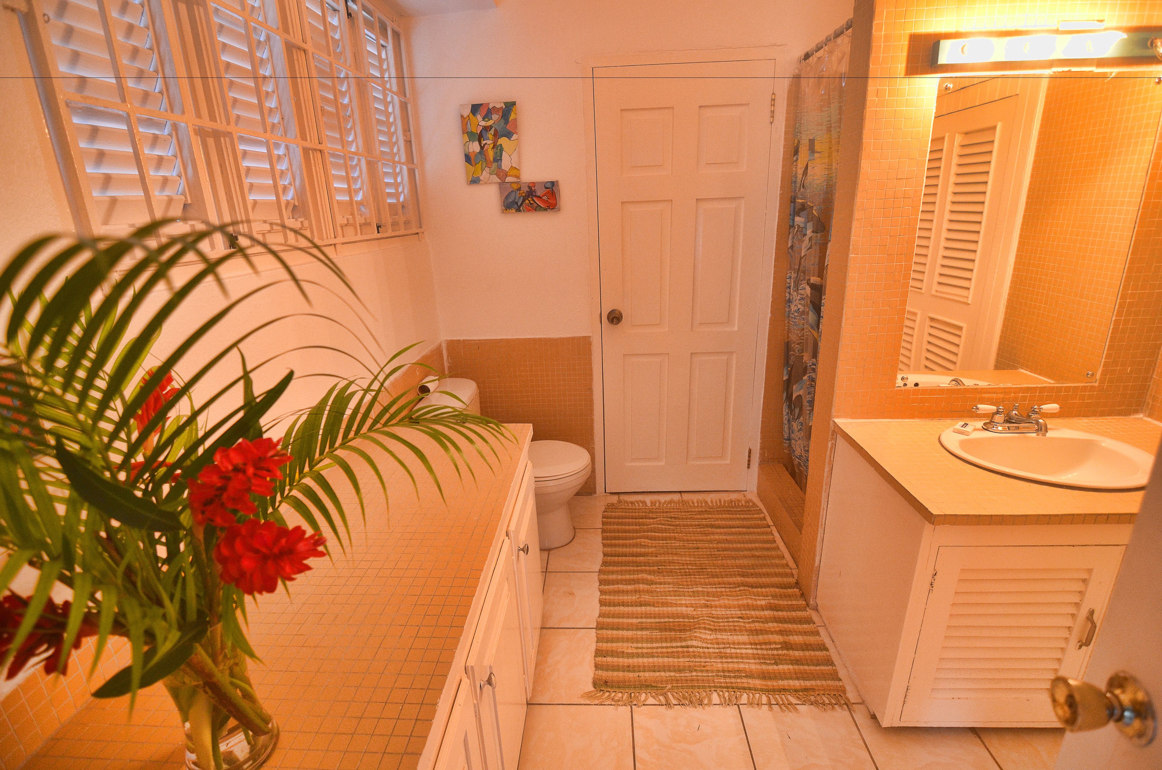 A bathroom with a toilet, sink, and shower. There is a door and a mirror.