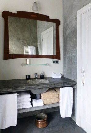 A bathroom with a marble sink, a large mirror, a towel rack, and a door. - Areias da Prainha (Sao Roque do Pico)