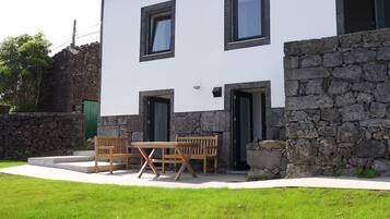 Une maison à deux étages, avec une façade en pierre et un revêtement blanc, dotée d’un patio aménagé avec des meubles en bois.