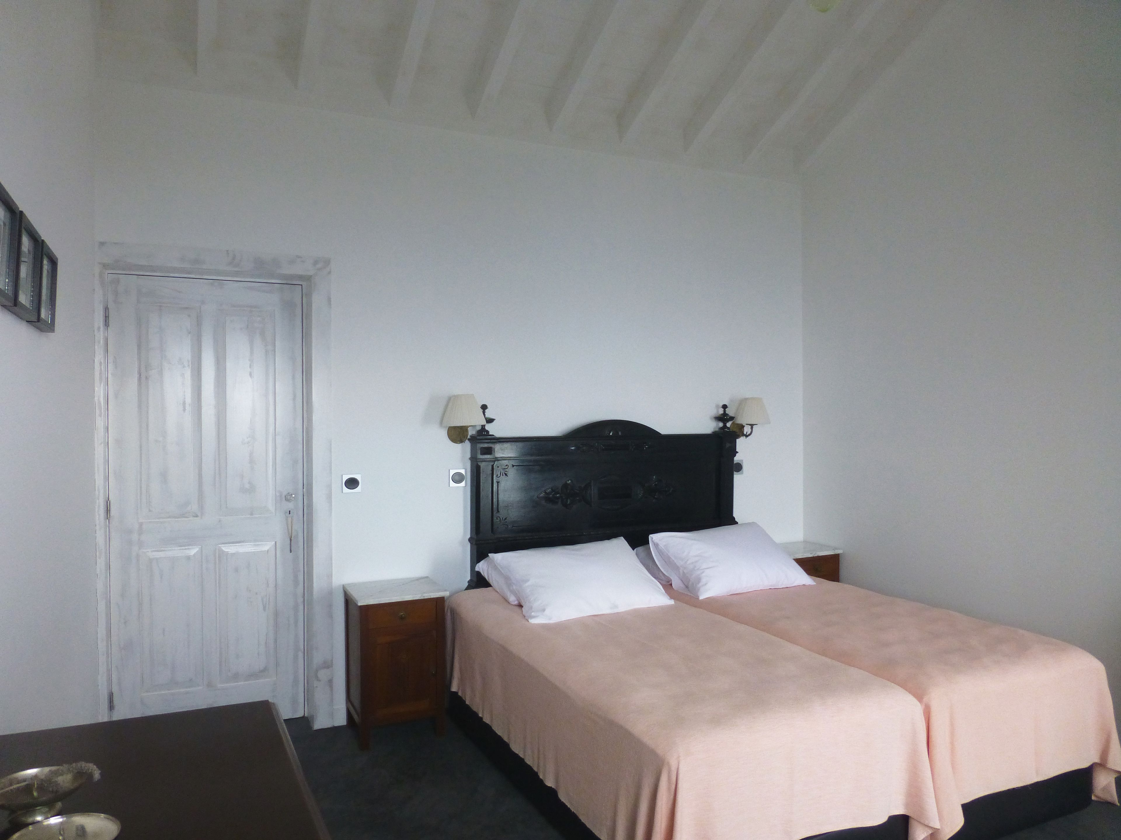 Une chambre à coucher avec deux lits, une tête de lit en bois, des lampes de chevet, une petite table de chevet et une porte blanche.