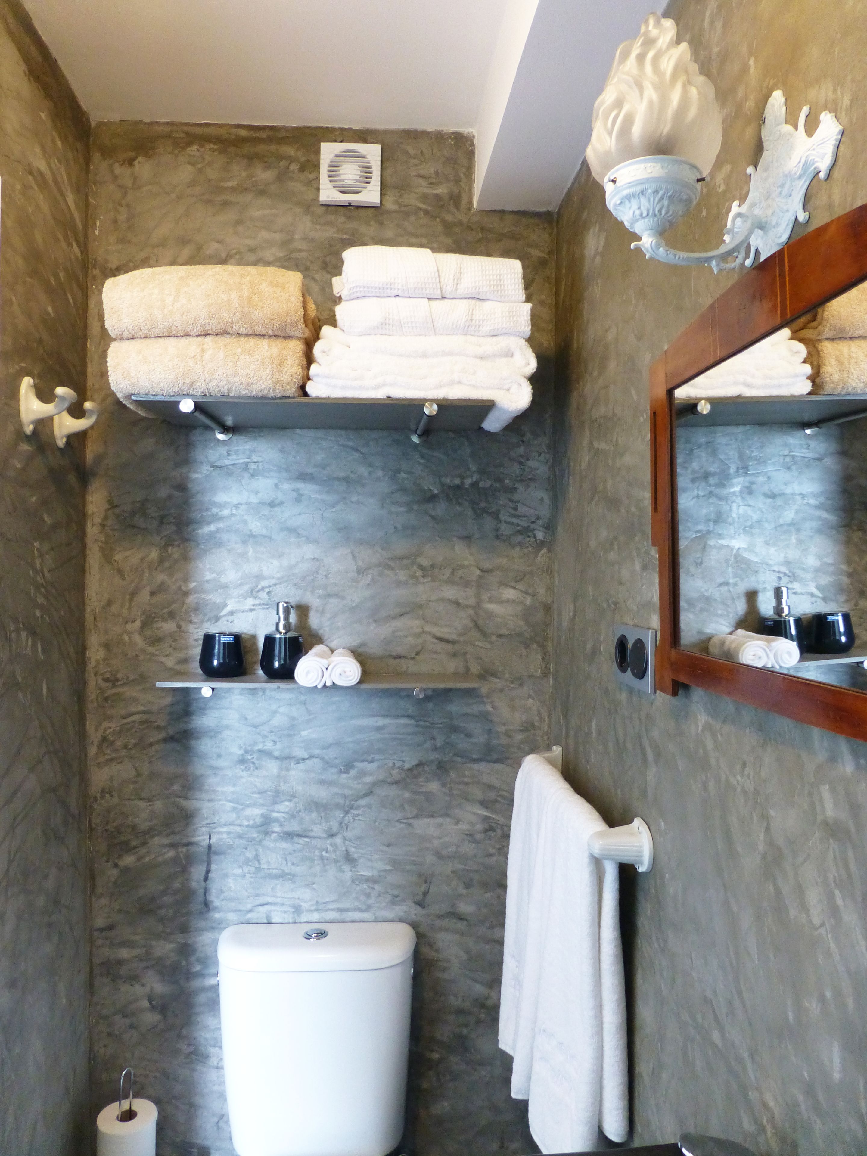 A bathroom with a stone wall, a toilet, a sink, and shelves holding towels and toiletries.