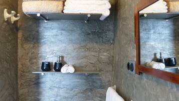 A bathroom with a stone wall, a toilet, a sink, and shelves holding towels and toiletries.