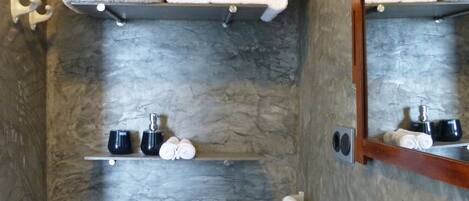 A bathroom with a stone wall, a toilet, a sink, and shelves holding towels and toiletries.
