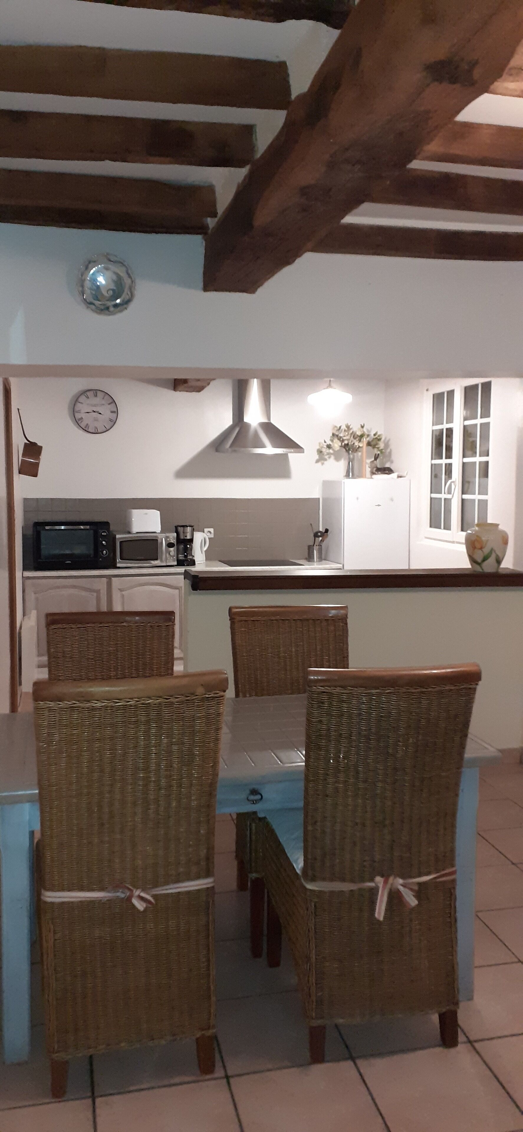 A dining area with wicker chairs and a table, a kitchen with a microwave and toaster, and a window with blinds.