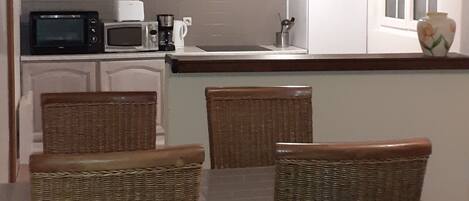 A dining area with wicker chairs and a table, a kitchen with a microwave and toaster, and a window with blinds.