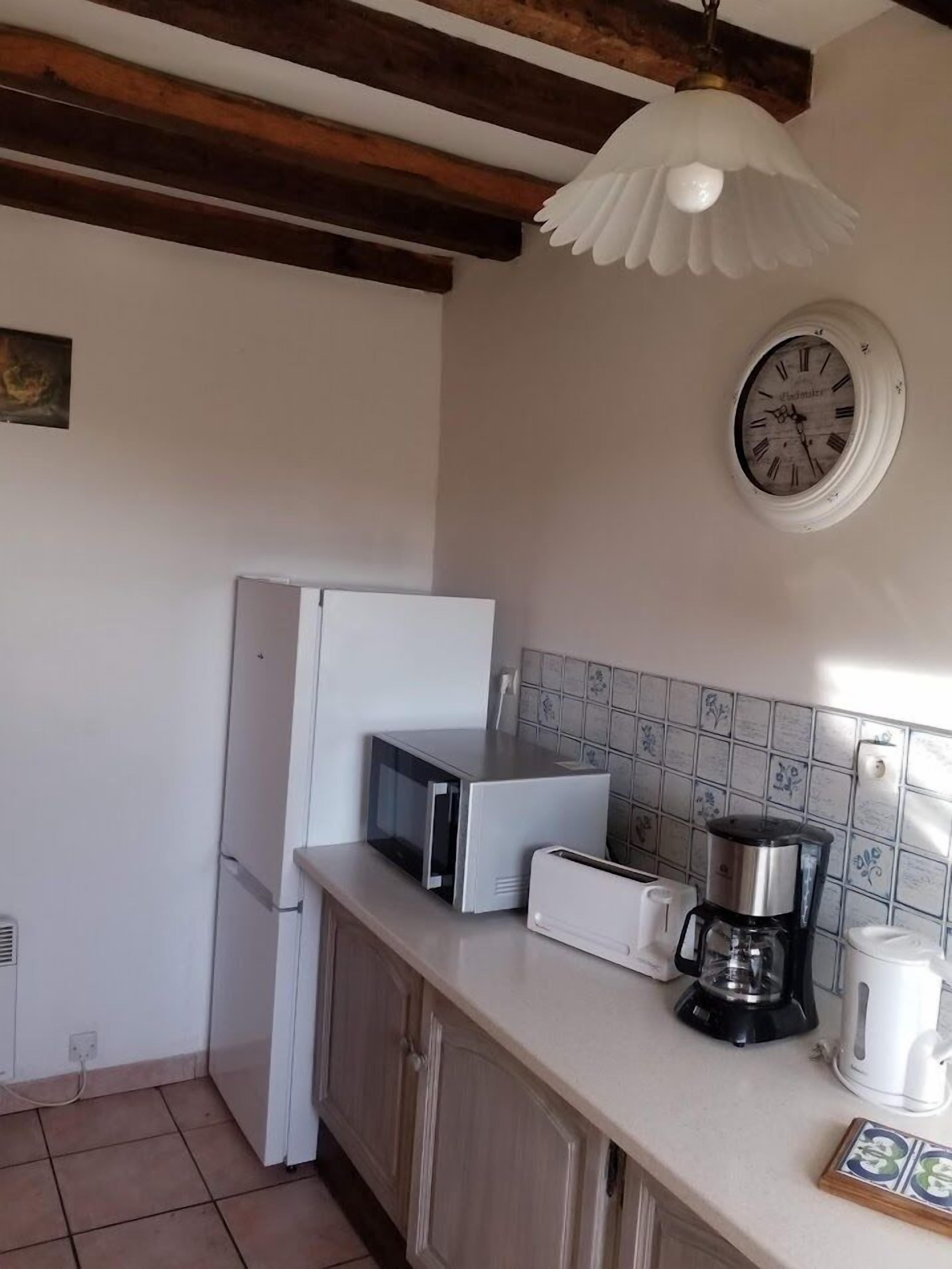 A kitchen with a white refrigerator, a microwave, a coffee maker, and a clock on the wall.