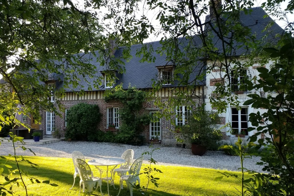 A two-story house with a brick facade, a gravel driveway, and a lawn with a table and chairs.