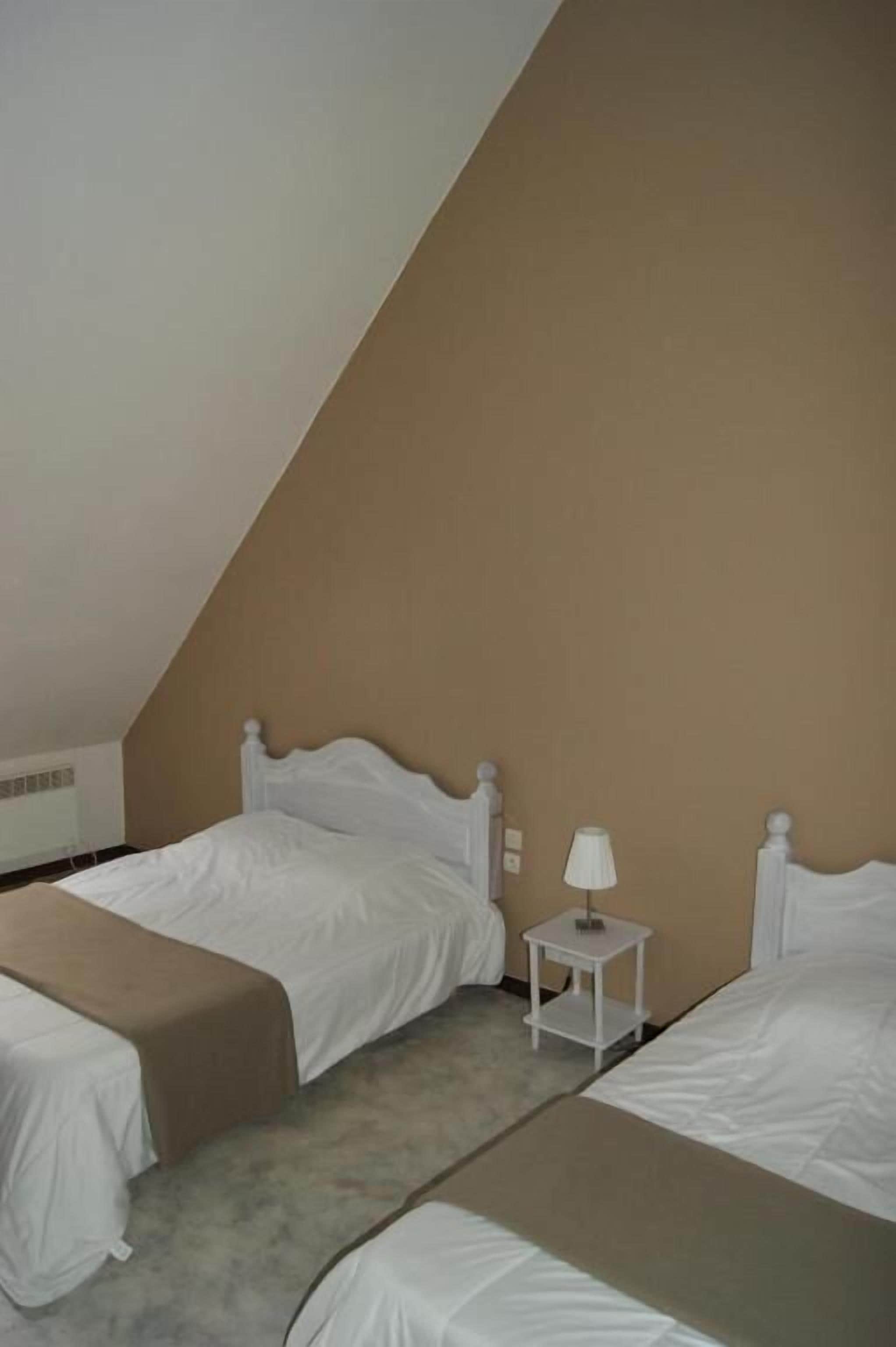 A small, triangular room with two beds, a bedside table with a lamp, and a beige wall.