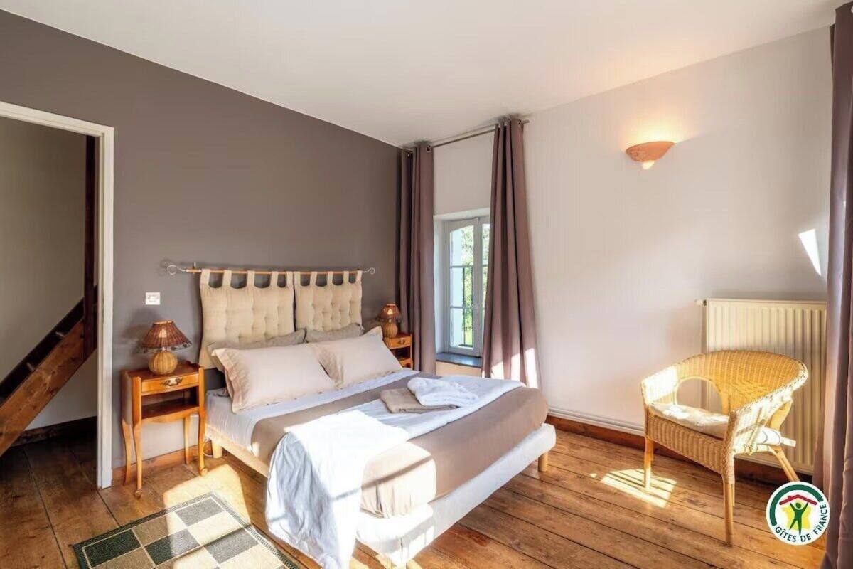 A bedroom with a bed, a nightstand, a chair, a window, and a radiator.