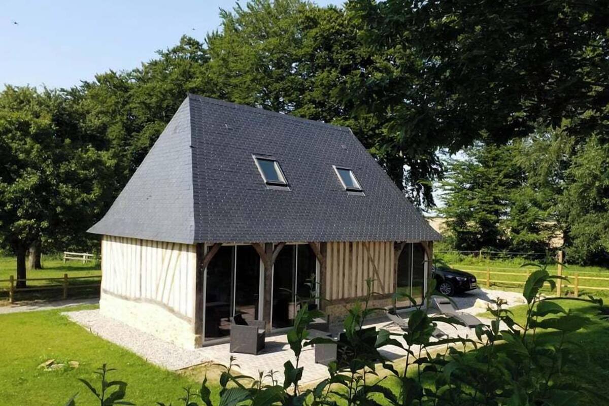 Ein kleines, eingeschossiges Haus mit Satteldach und zwei kleinen Fenstern. Es ist von einem gepflegten Rasen und Bäumen umgeben.