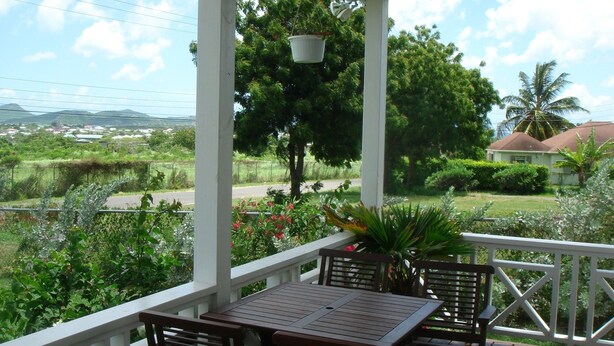 A covered outdoor area with a table and chairs, surrounded by greenery and a view of a residential area. - Friars Hill Cottage (St. John's)