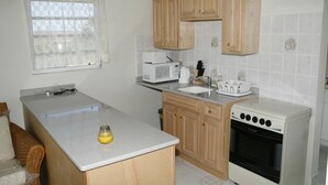 A kitchen with wooden cabinets, a microwave, a sink, and a stove. - Friars Hill Cottage (St. John's)