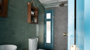 Une salle de bain avec un lavabo, des toilettes et une douche, tous de couleur blanche, une étagère en bois et une poubelle.