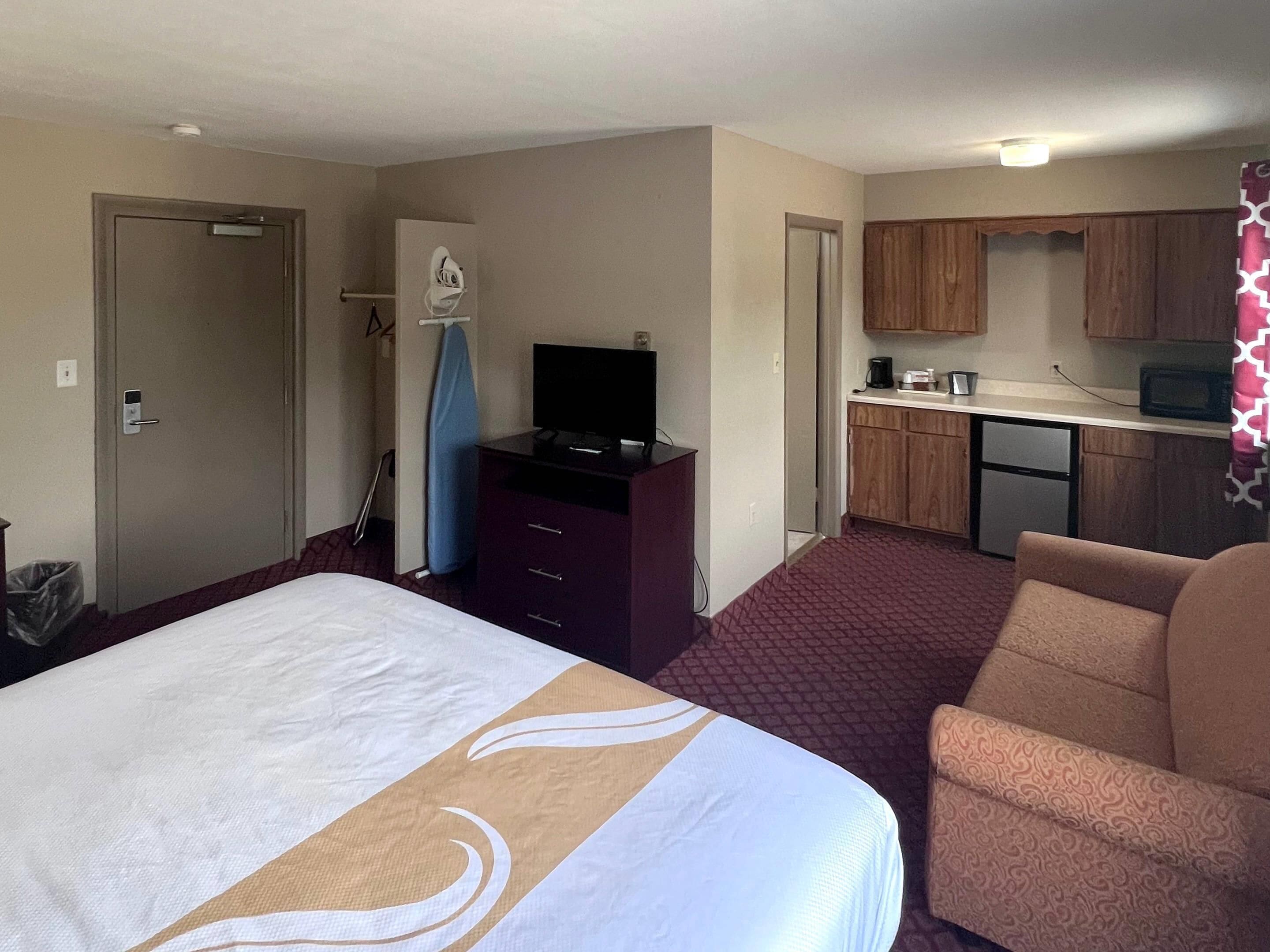 Habitació d'hotel amb llit, escriptori amb televisió, petita cuina i una cadira.