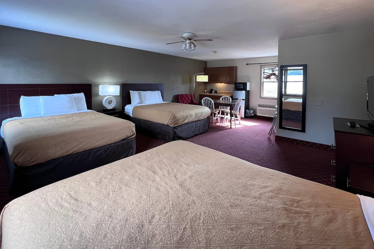 A hotel room with two beds, a desk, a chair, a microwave, and a television.
