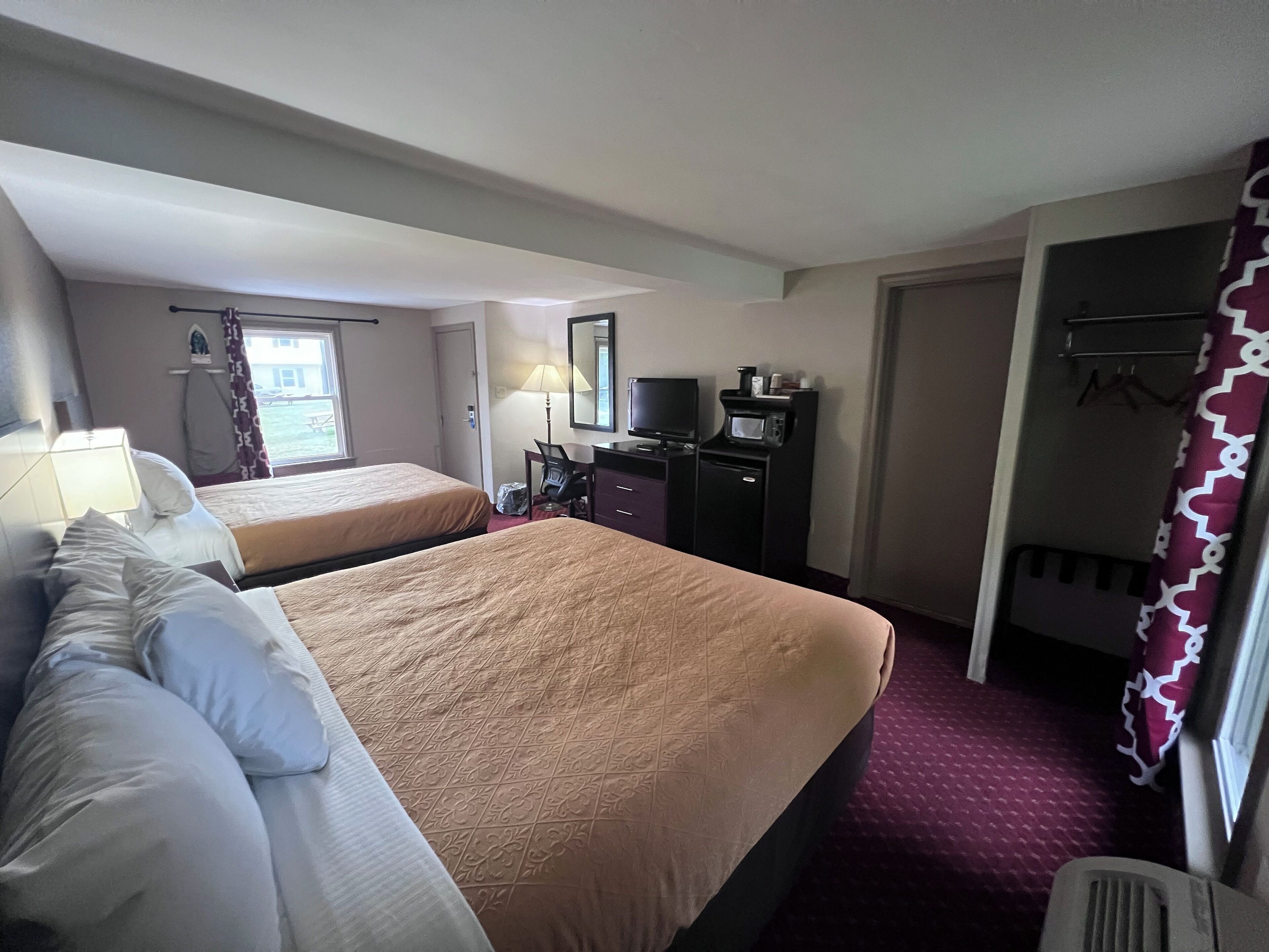 A hotel room with two beds, a desk with a computer, a TV, and a microwave.