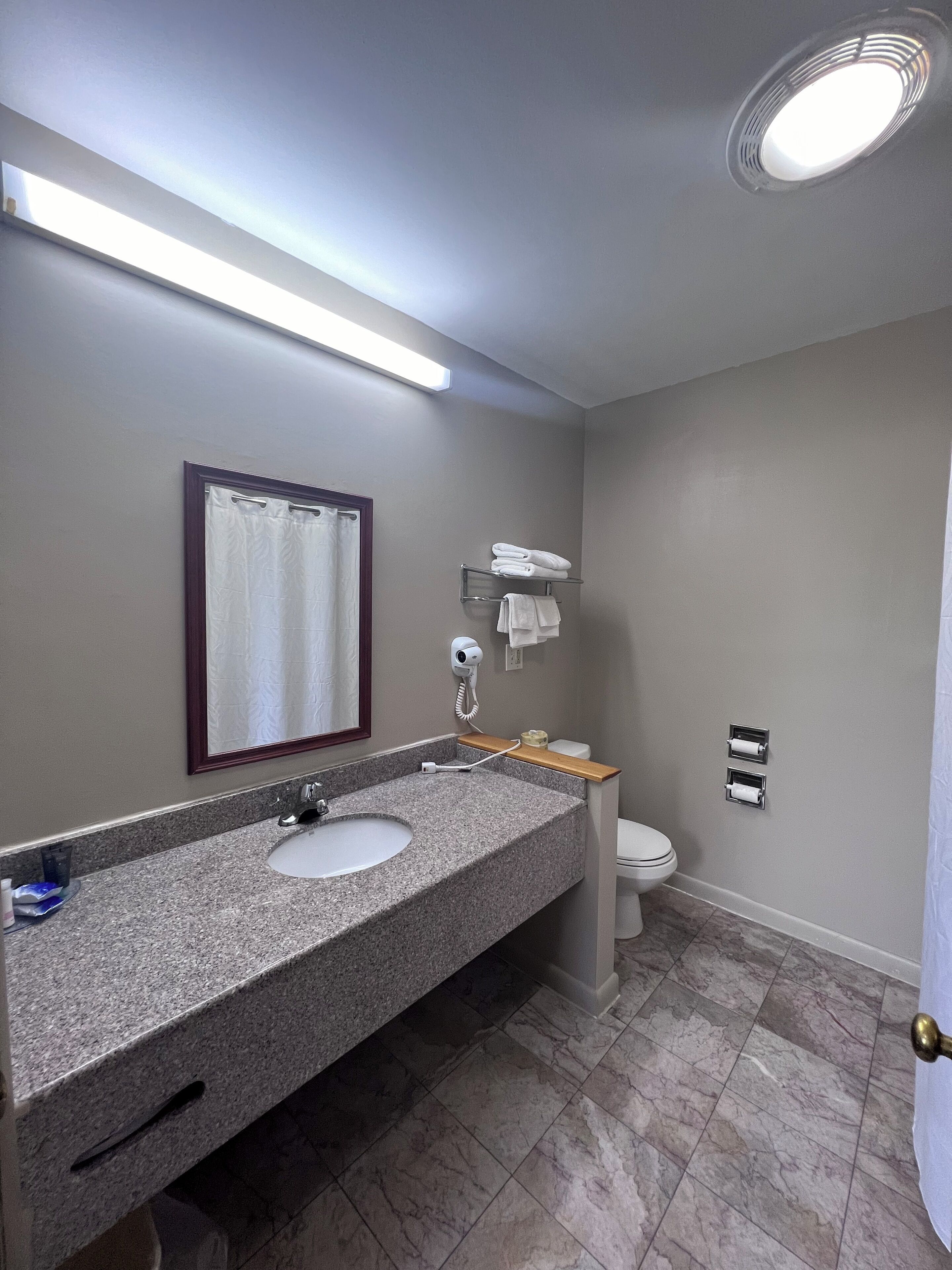 Un baño con lavamanos de granito, un espejo, toallero, inodoro y cortina de ducha.