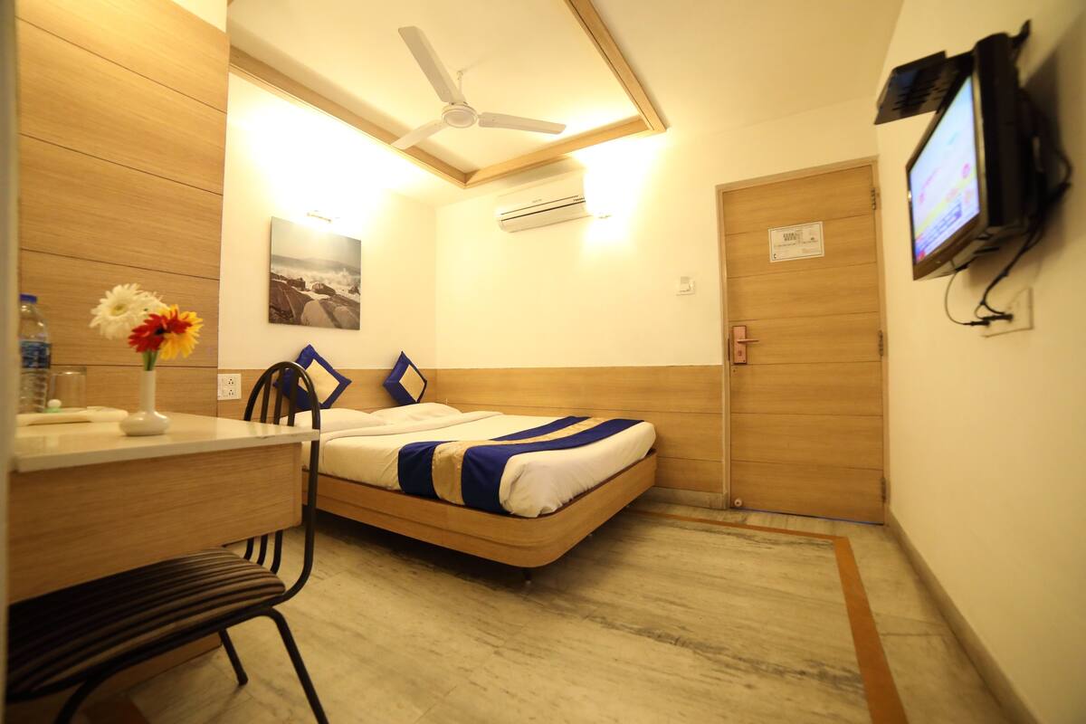 A compact hotel room with a bed, a desk, a chair, a television, and a ceiling fan.