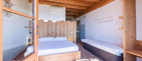 A wooden room with a bed, a bench, and a wall with a quote.