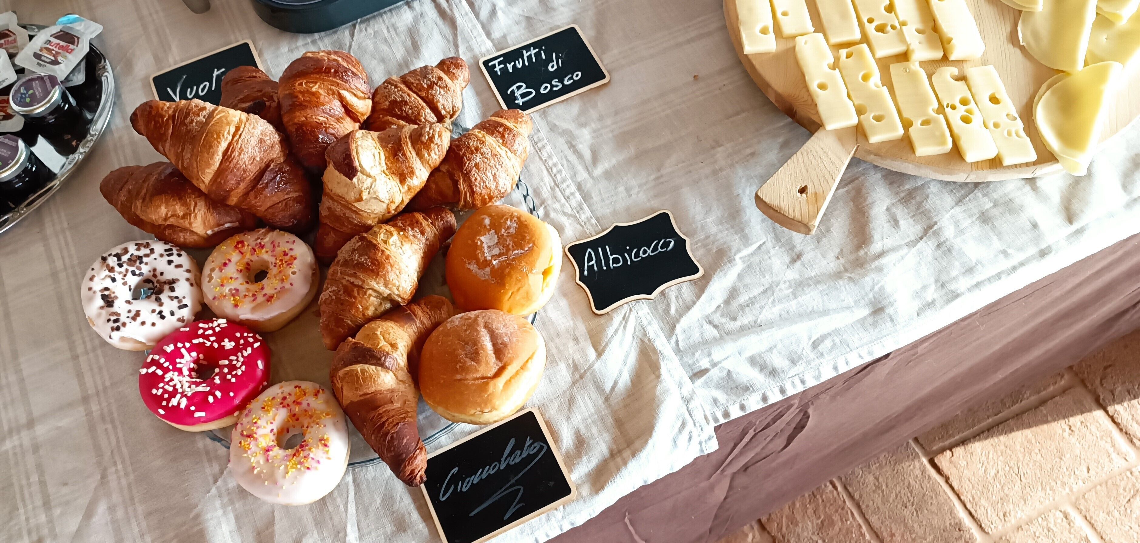 A variety of pastries and cheeses on a table with labels indicating types like 'Vuot,' 'Albicocco,' and 'Ciacchibatta.'