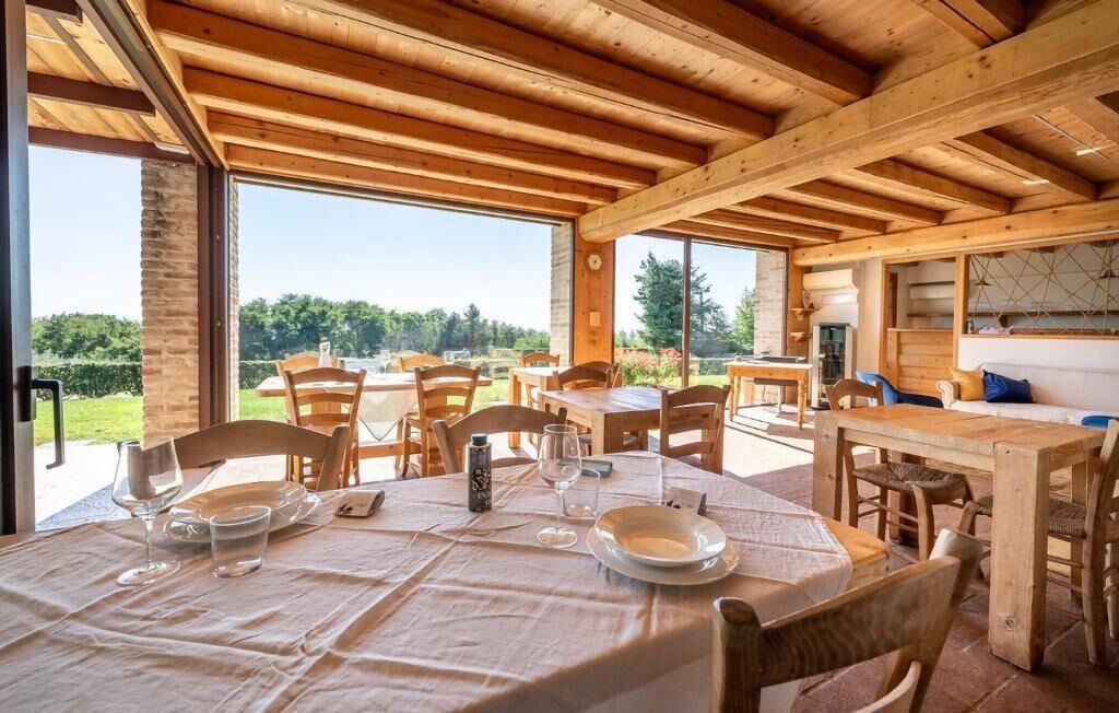 A wooden dining area with tables and chairs, large windows, and a view of greenery.