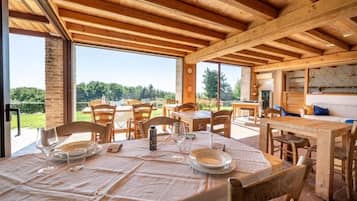 A wooden dining area with tables and chairs, large windows, and a view of greenery.