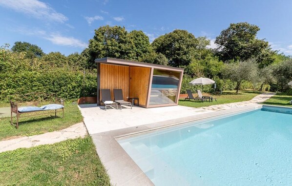 A modern outdoor pool area with a glass-enclosed cabana, lounge chairs, and a small table with an umbrella. - Agriturismo Dolce Colle (Volpago del Montello)