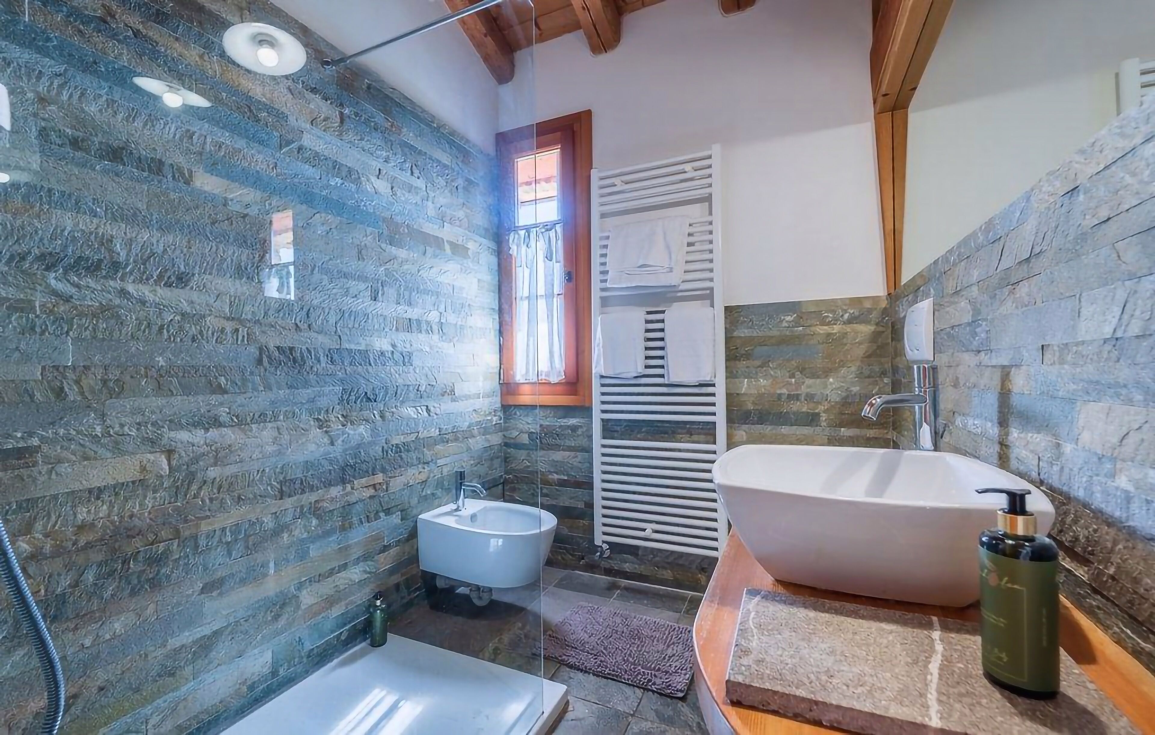 A bathroom with a stone wall, a freestanding bathtub, a pedestal sink, and a bidet.