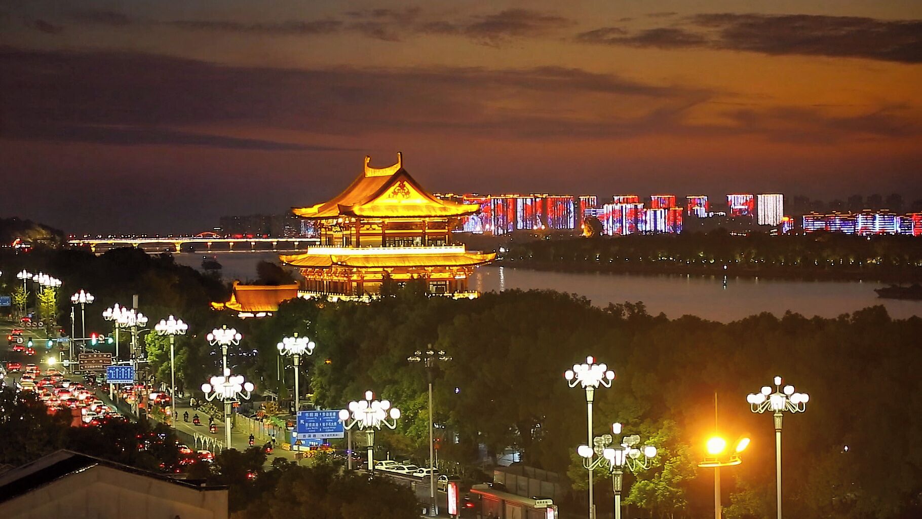 A traditional building with a golden roof, surrounded by modern city lights and a river.