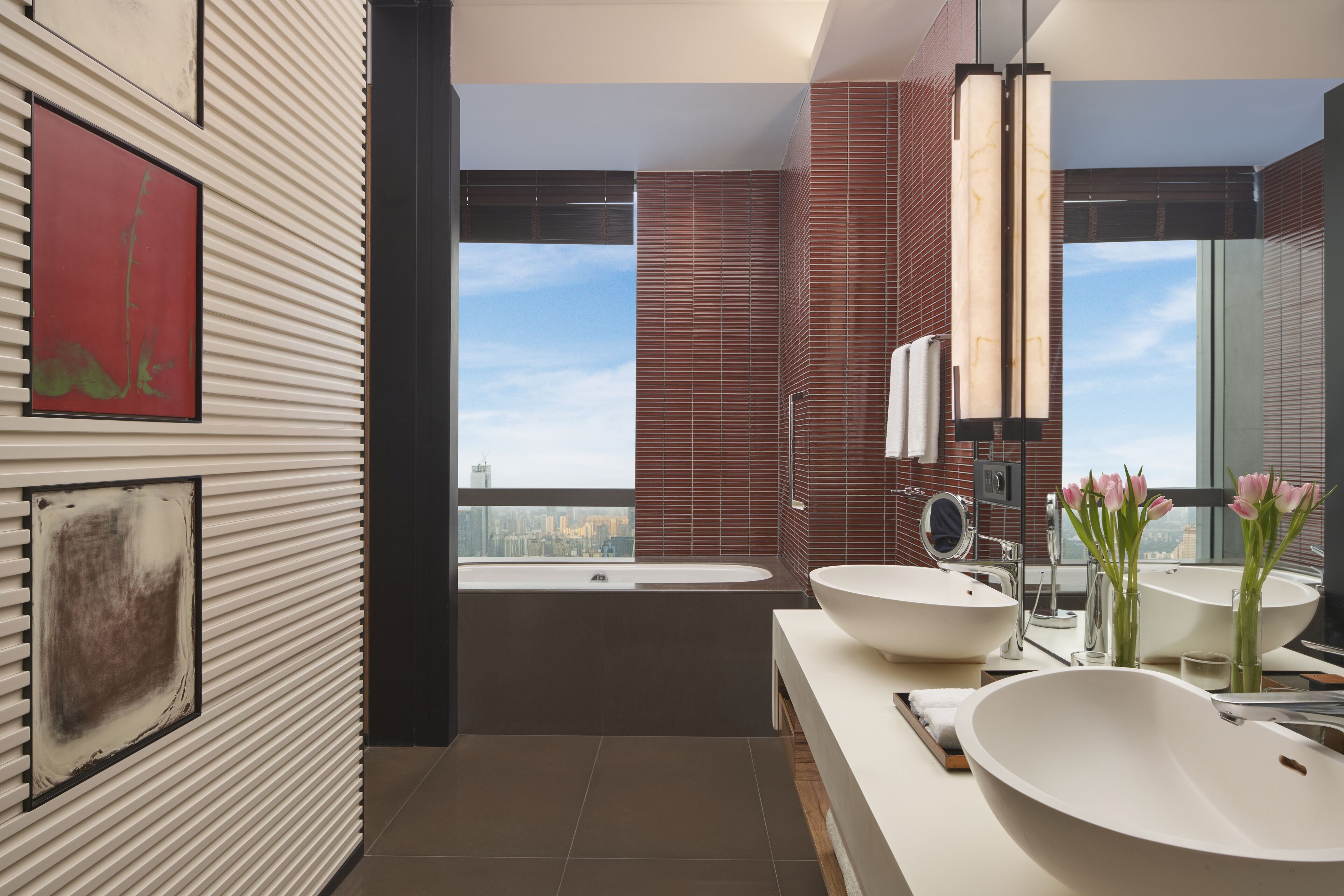 A modern bathroom with two large sinks, a bathtub, and a city view.