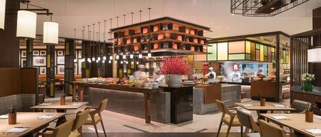 A modern restaurant with a central island, multiple dining tables, and a variety of seating options.