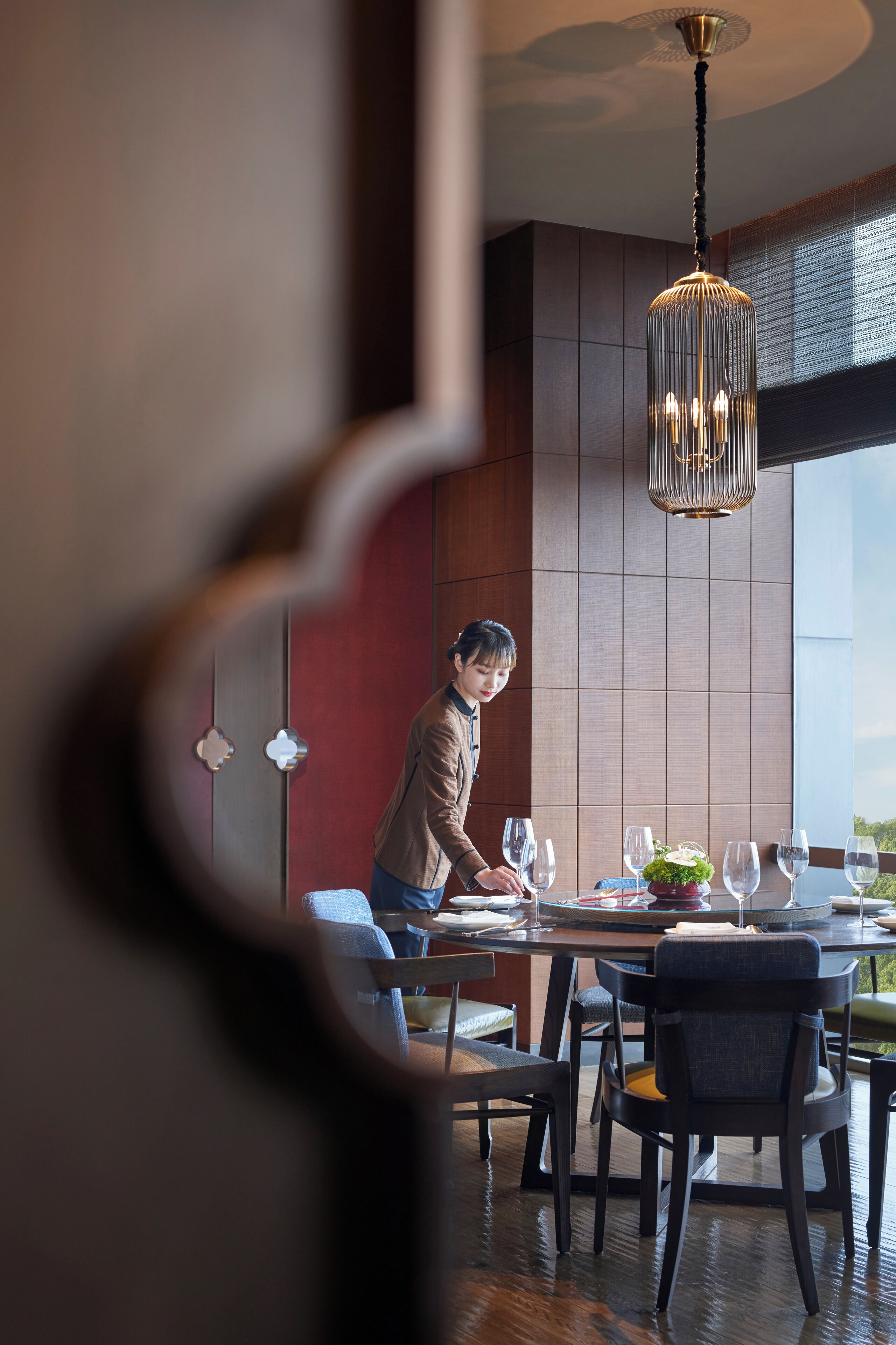 Un coin repas avec une table dressée pour deux personnes, une personne qui prépare un repas et un lustre moderne.