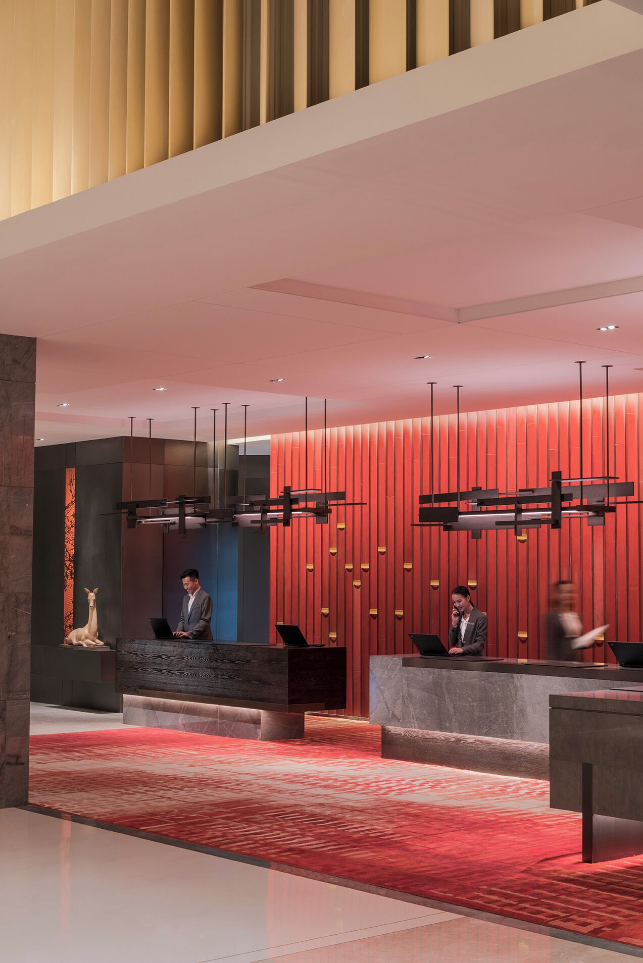 A modern reception area with a red and beige color scheme, featuring a reception desk, seating area, and a decorative wall with vertical panels.