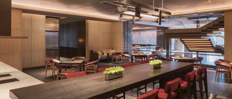 A modern dining area with a long table, red upholstered chairs, and a central plant.