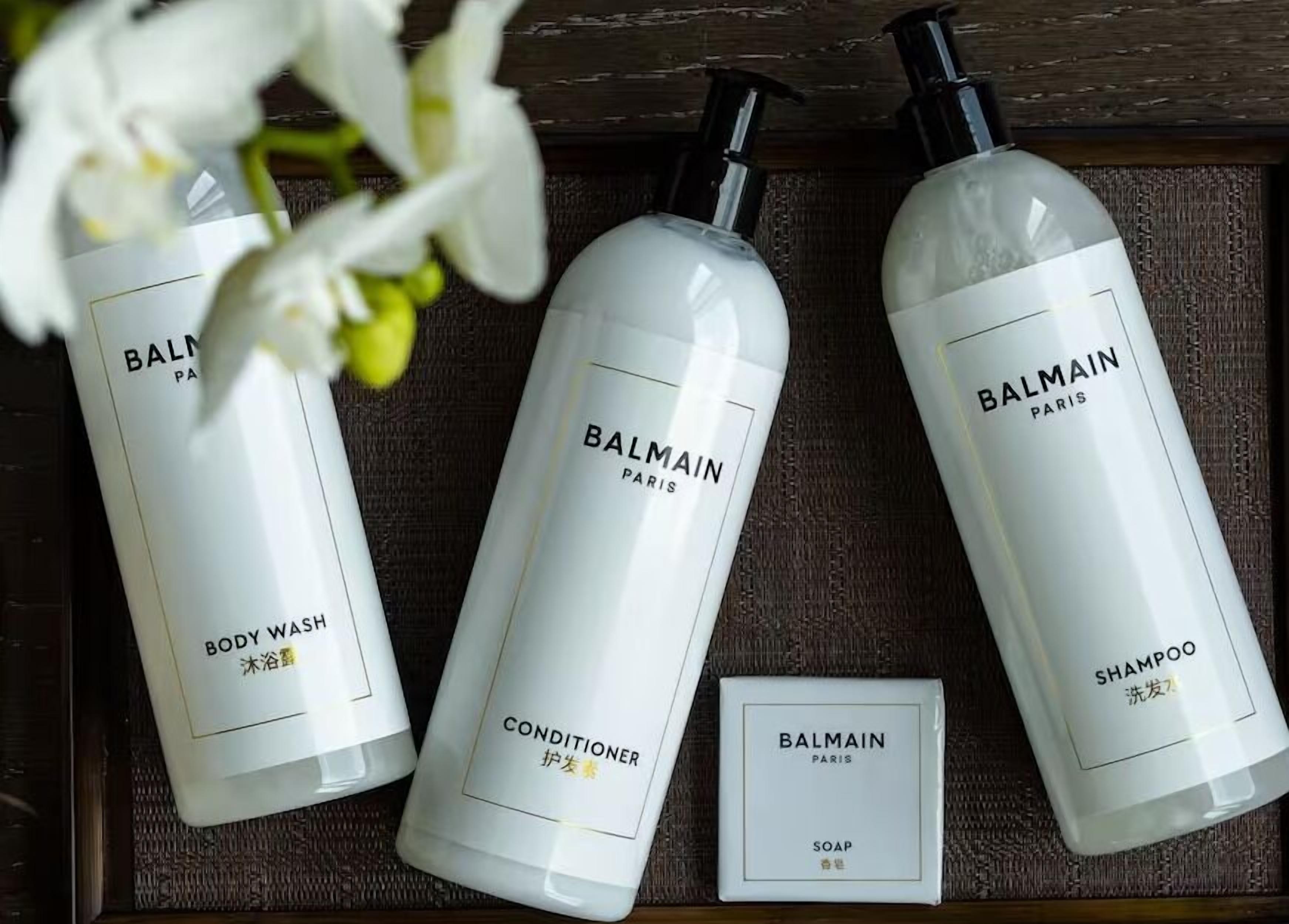 Three bottles of Balmain Paris body wash, conditioner, and shampoo, along with a soap bar, all placed on a wooden surface.