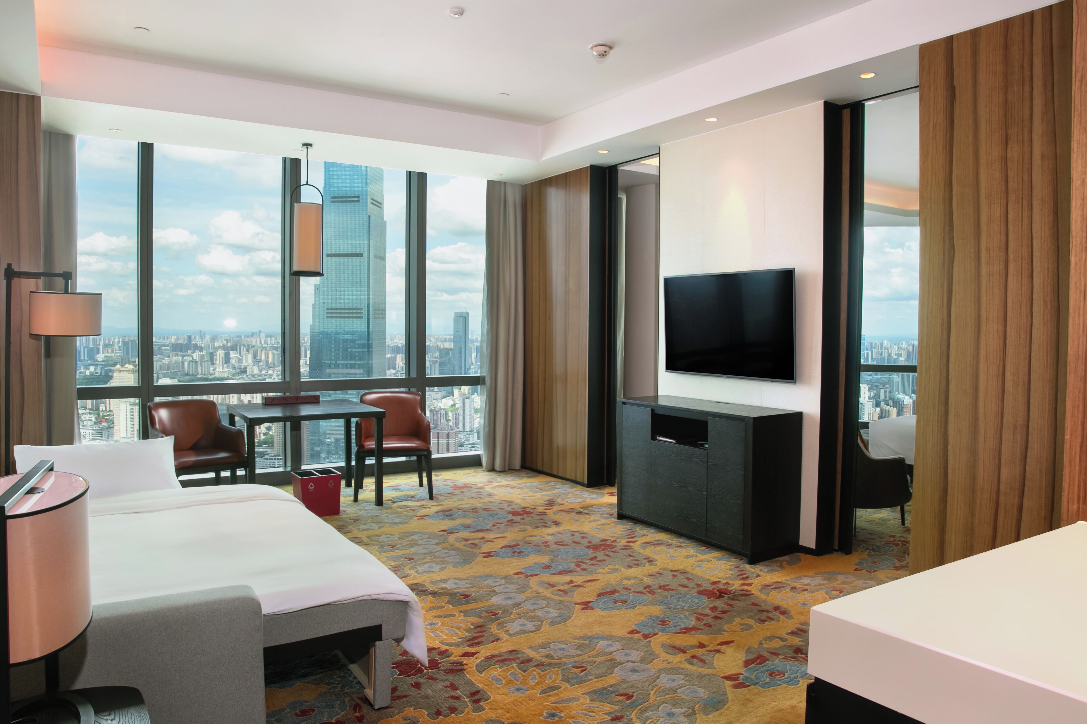 Une chambre d’hôtel équipée d’un lit, d’un bureau, d’une chaise, d’une télévision et d’une grande fenêtre donnant sur la ville.