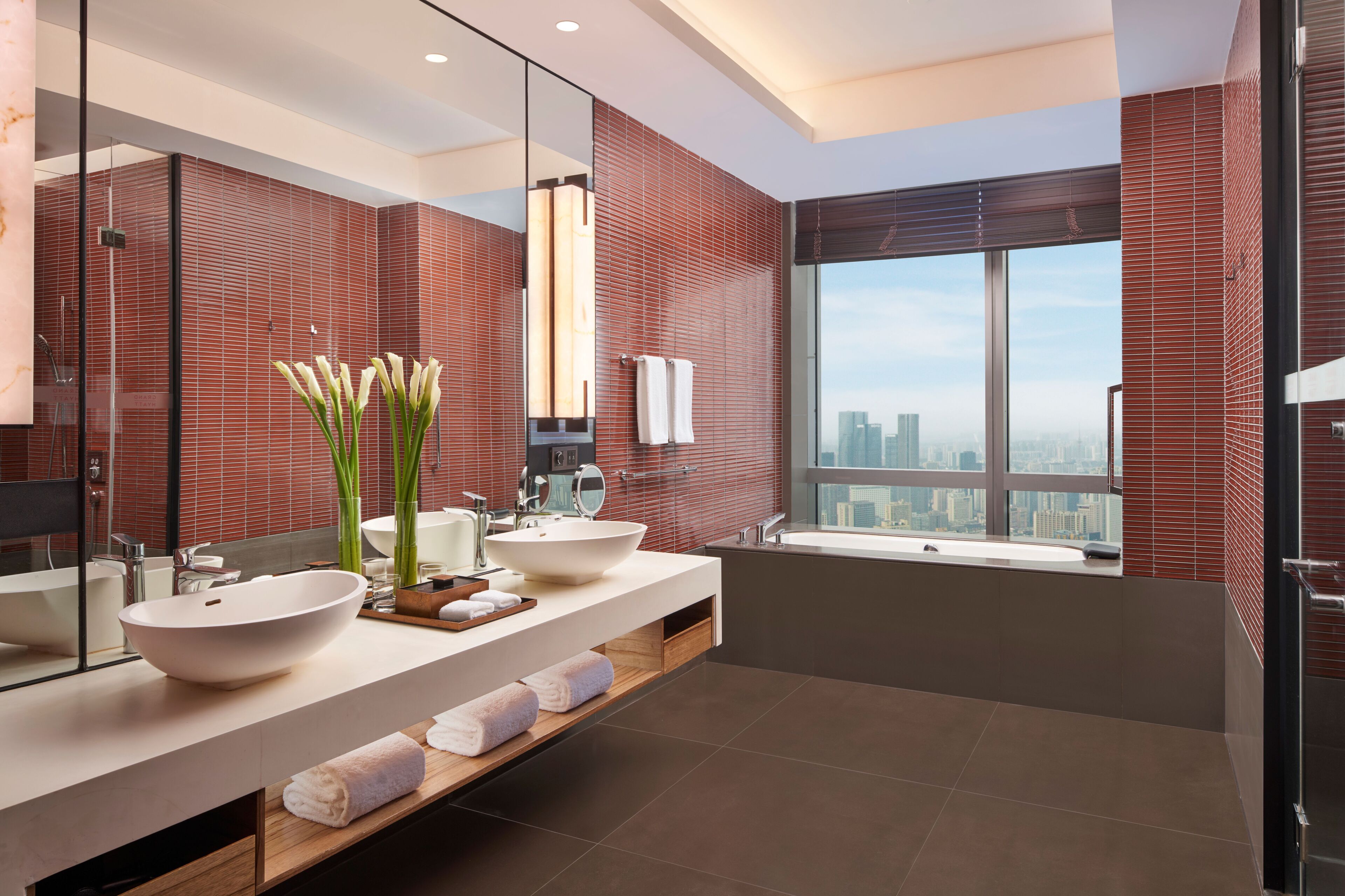 A modern bathroom with a large mirror, two sinks, a bathtub, and a view of the city.