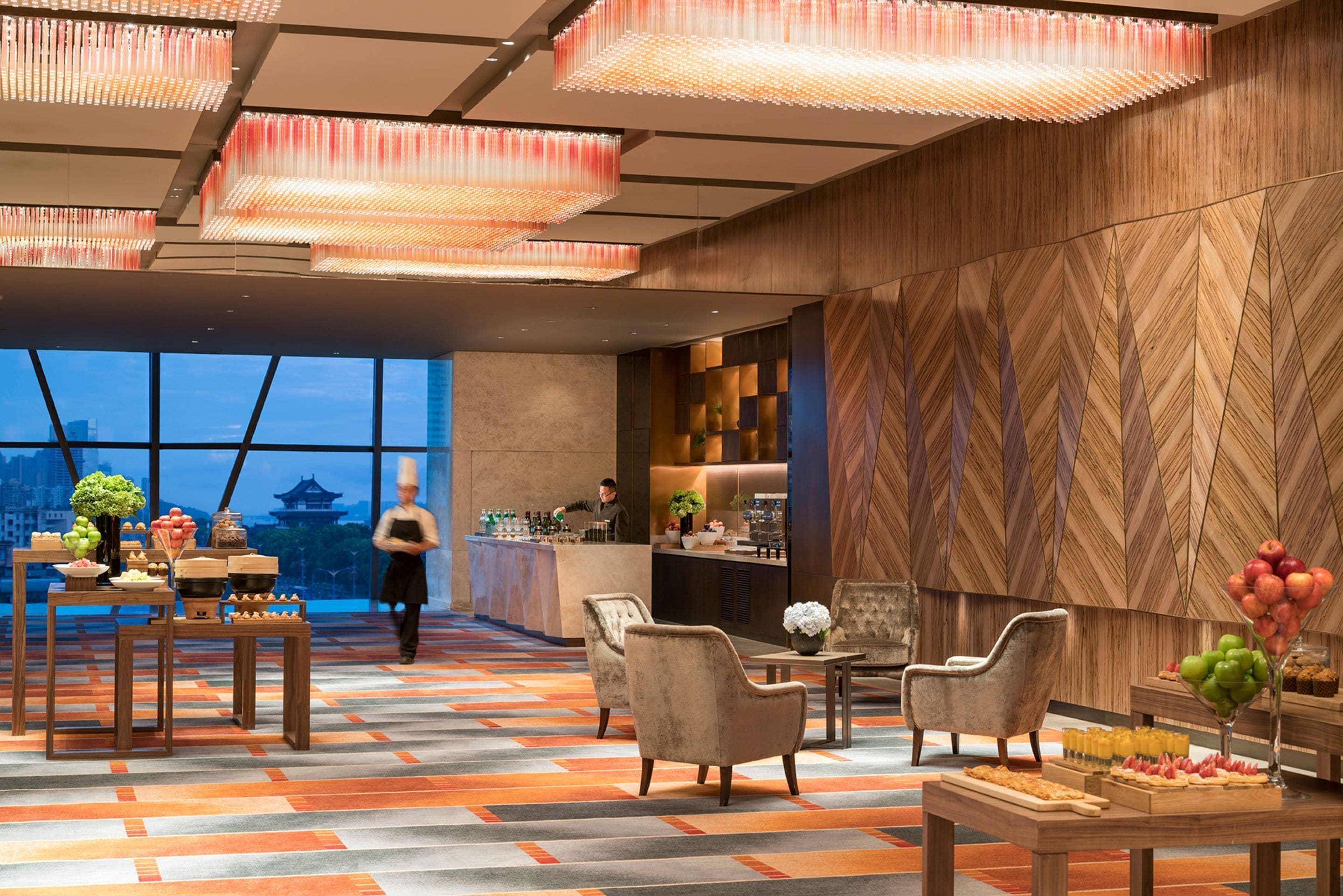 A modern hotel lobby with a bar area, seating, and a view of a cityscape.