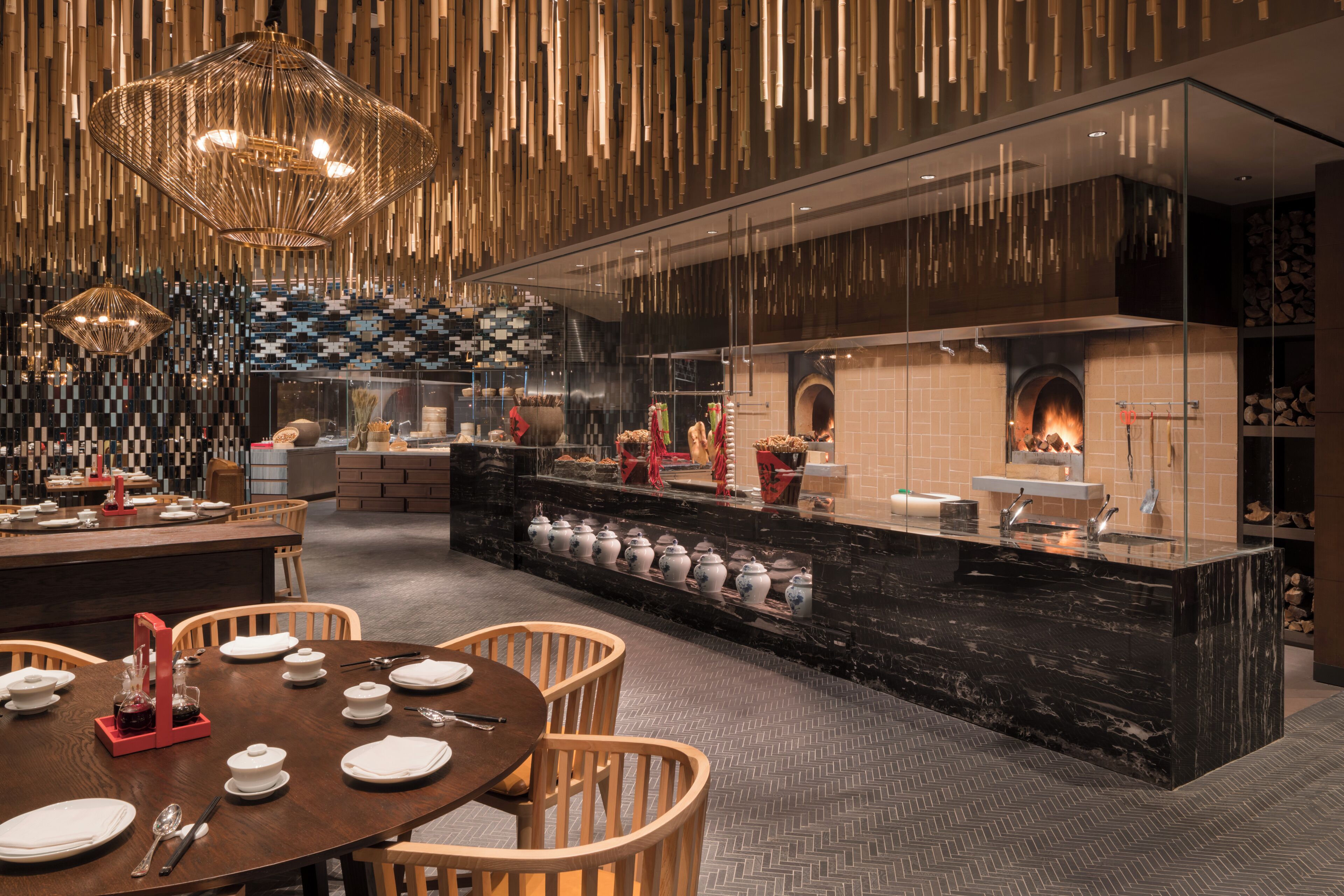 A modern restaurant with a central island, wooden chairs, and hanging light fixtures.